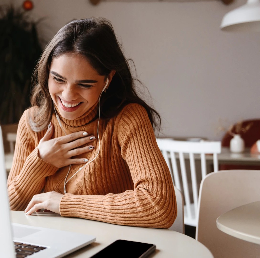Mulher sorrindo com fones de ouvido assistindo a uma aula online de autocompaixão - Curso Em Paz Comigo
